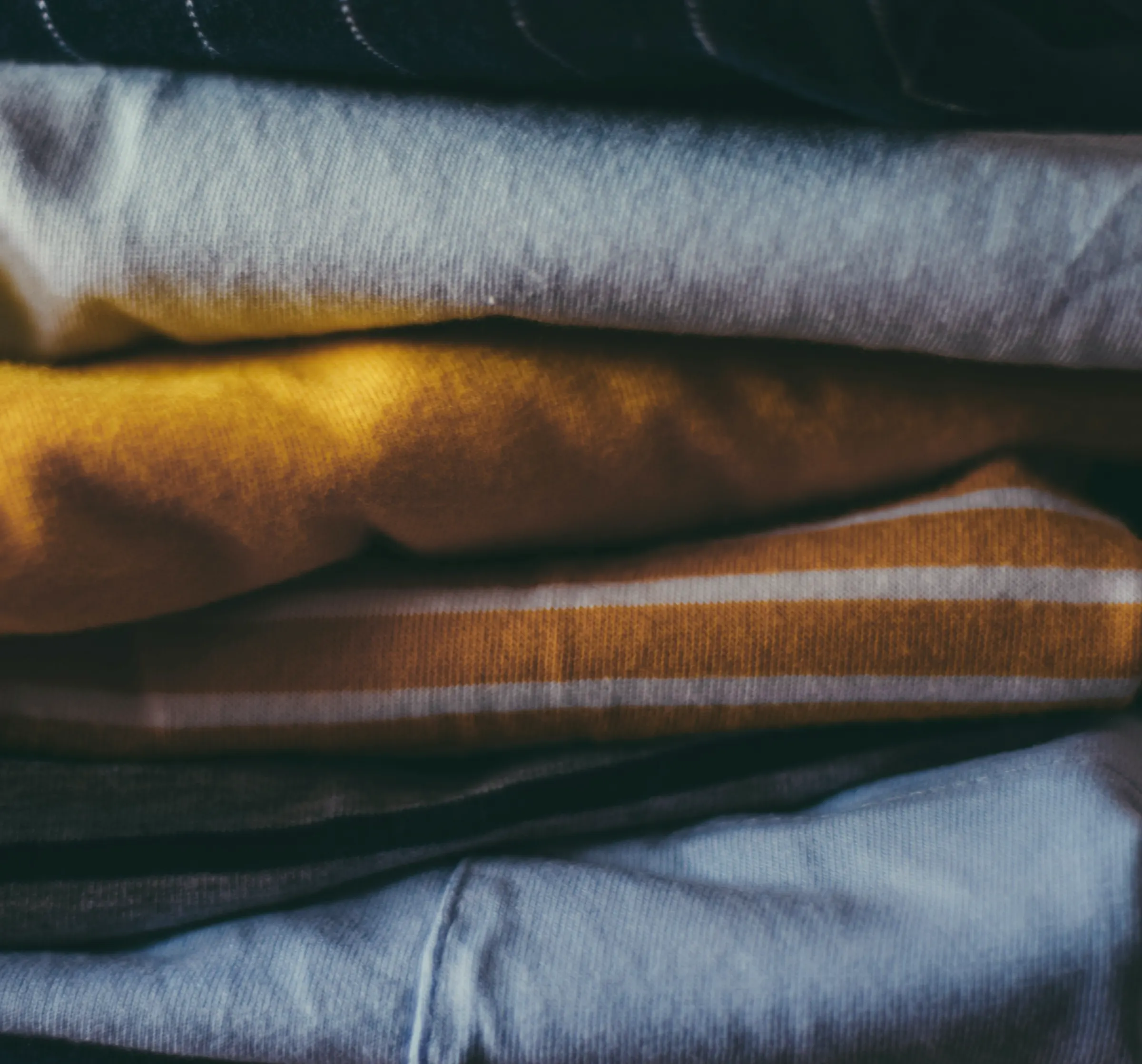 A tight stack of folded garments in powder blue, mustard, rust stripe and denim