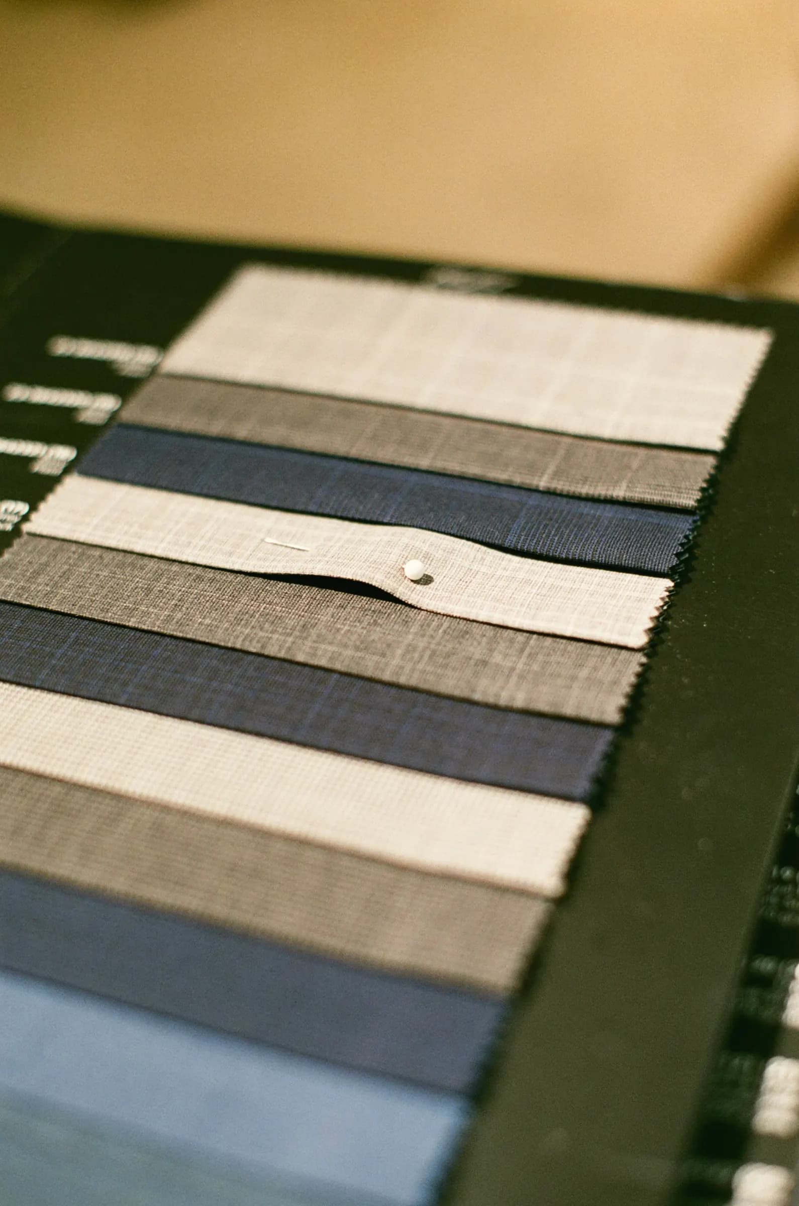 A tailoring swatch book with fanned suiting cloth strips in cream, grey and navy