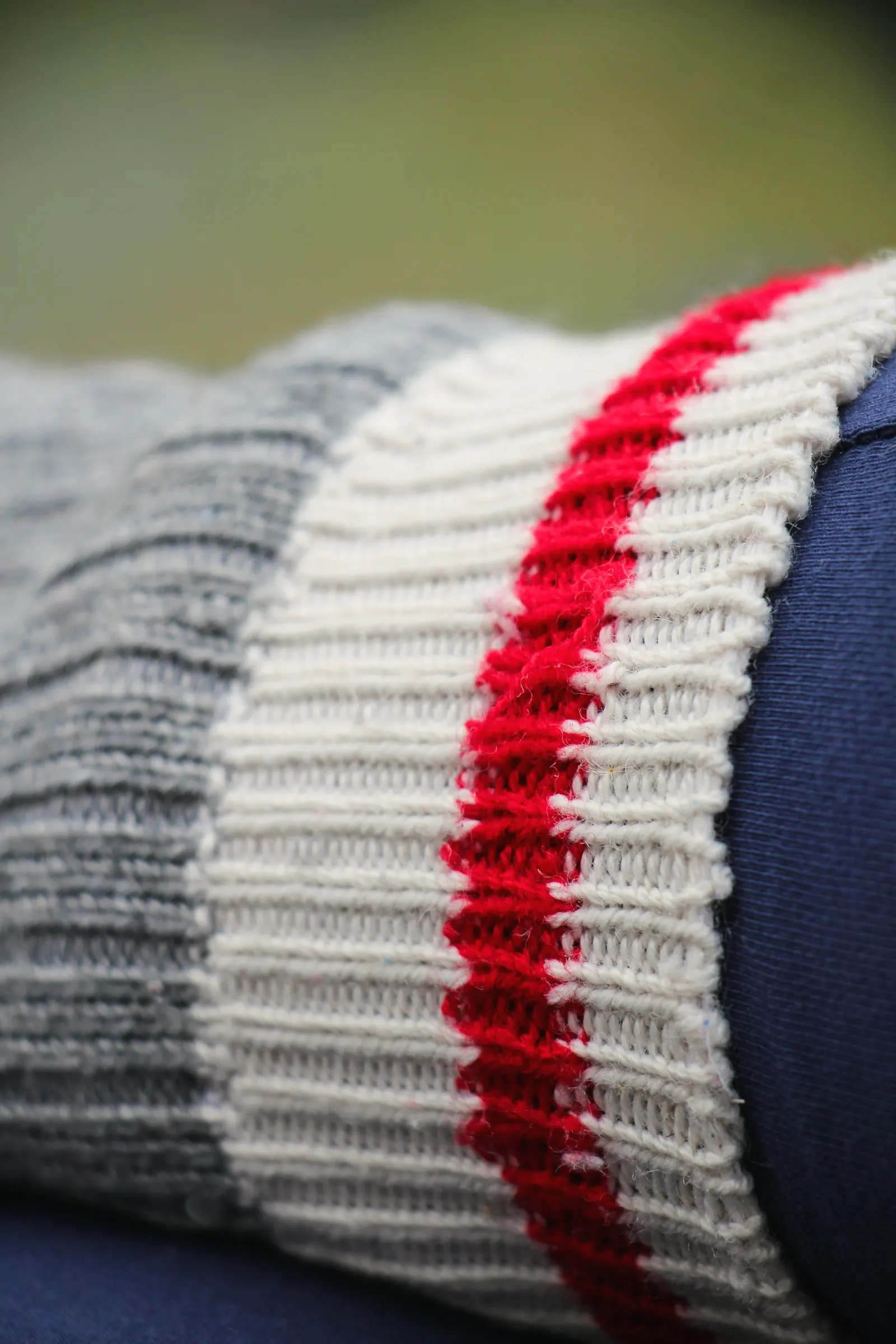 Close-up of a grey and cream rib-knit cuff with a red varsity stripe over navy